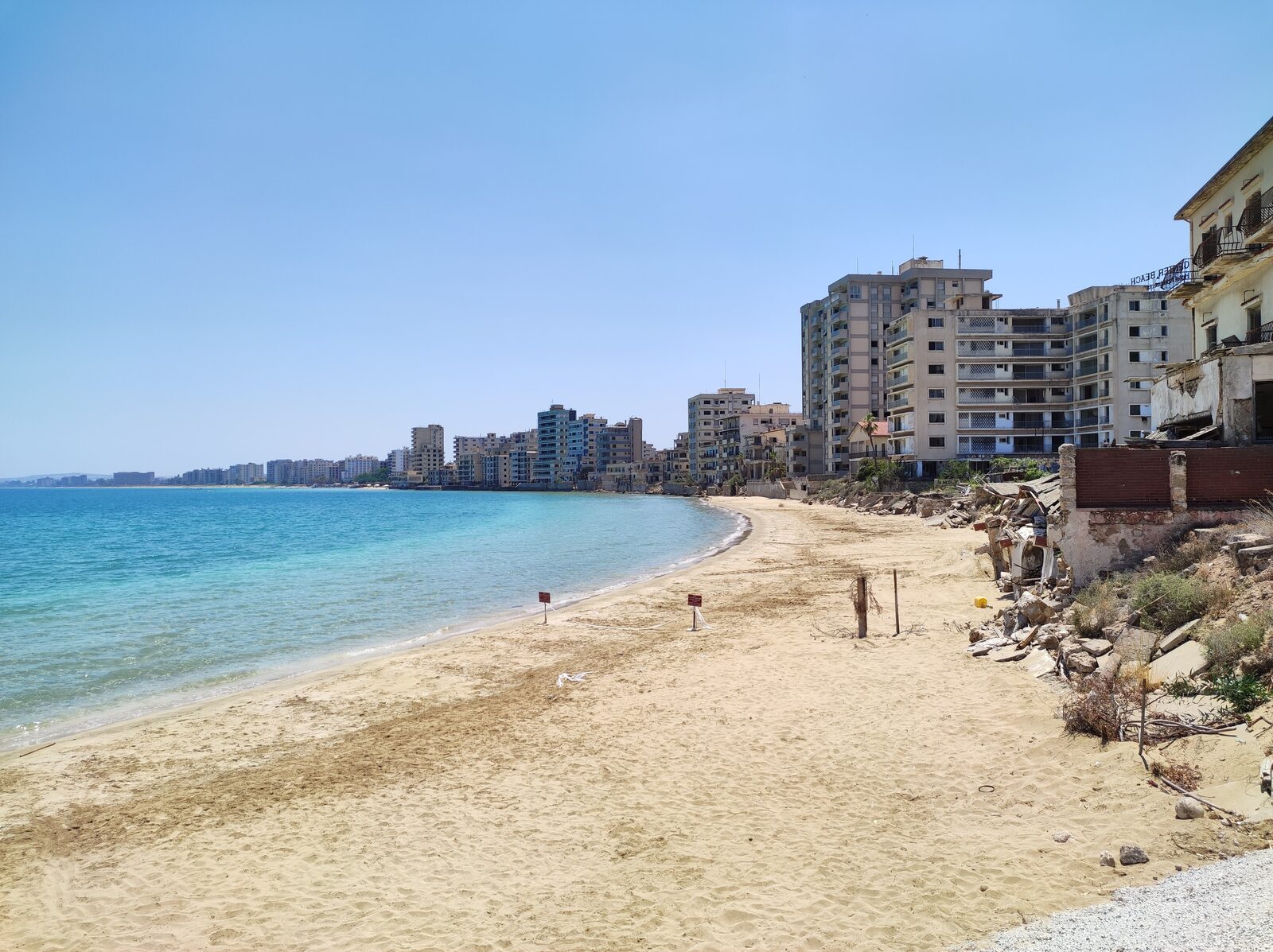 Leżaki i kąpiący się na plaży w Varosha, na brzegu pusty wieżowiec hotelowy