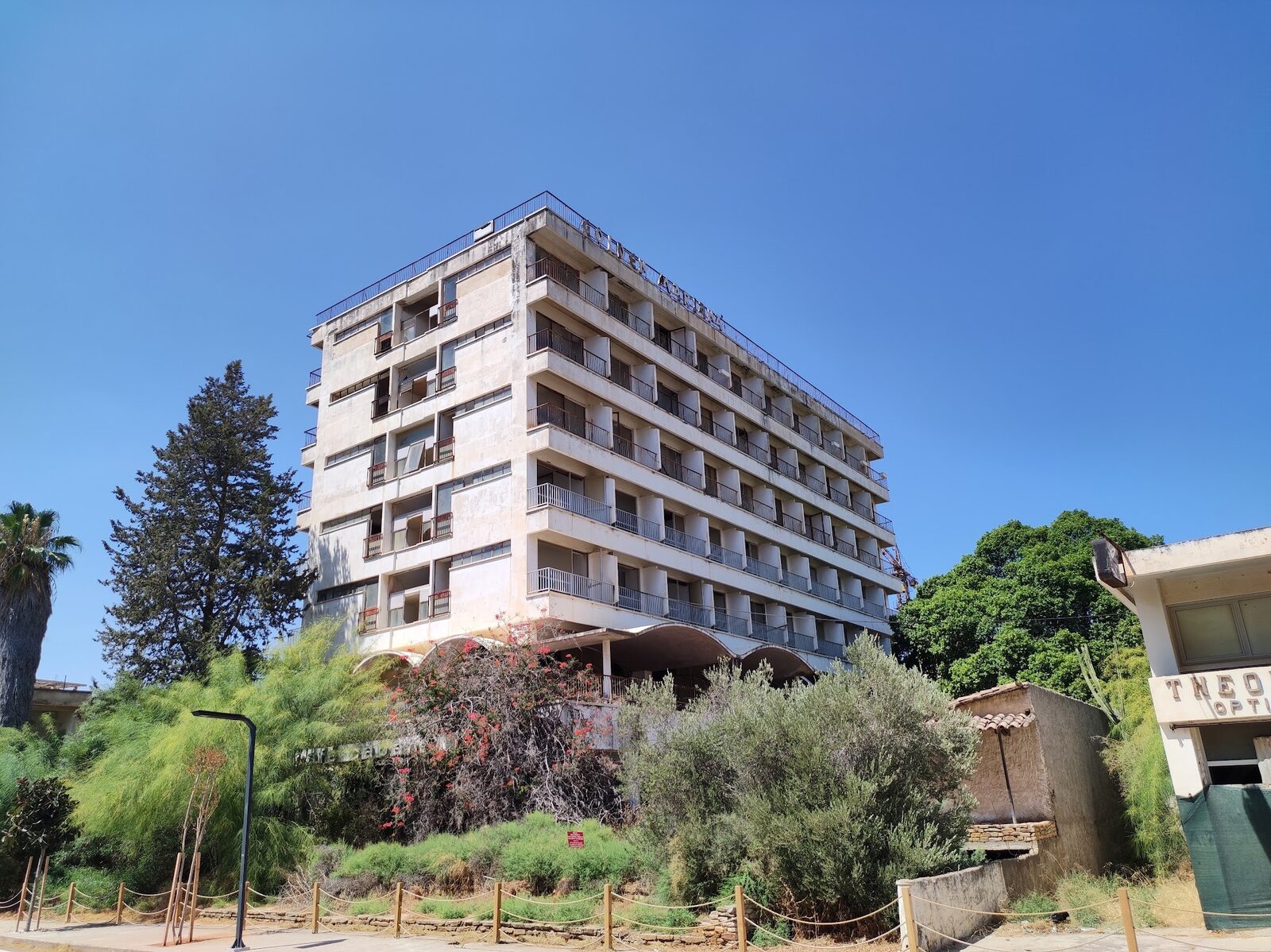 Pusty siedmiopiętrowy hotel w Varosha za zarośniętymi krzakami i ogrodzeniem z liny