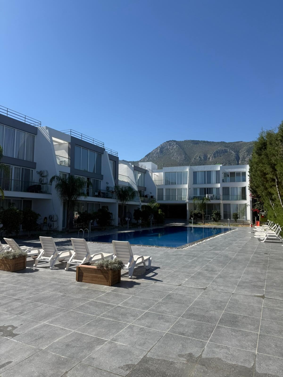 Coliseum Court complex: pool, sun loungers and building facade against the Pentadaktylos mountains