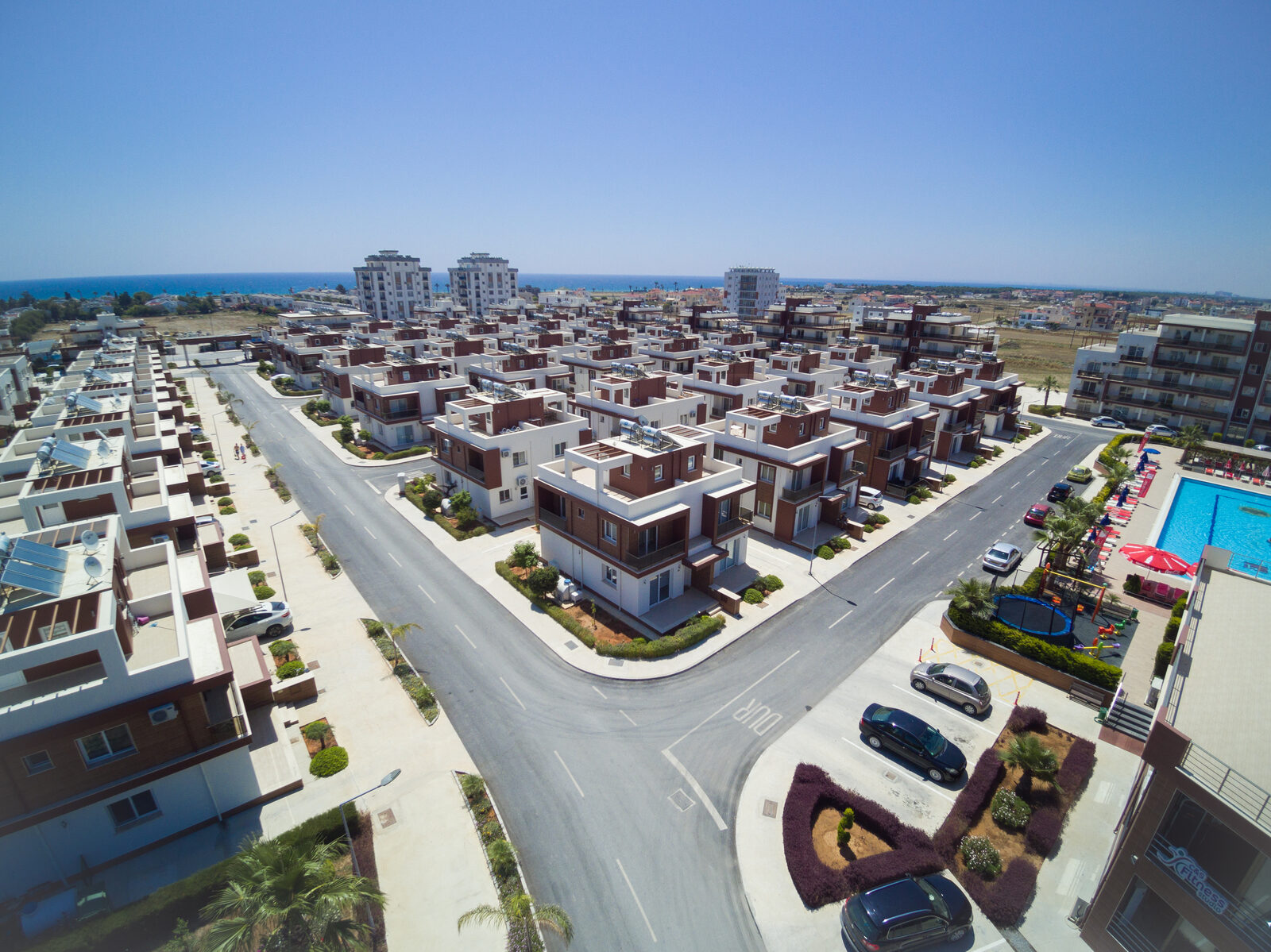 Streets of the complex from above: villas, a pool with parasols, a children's playground and the fitness centre