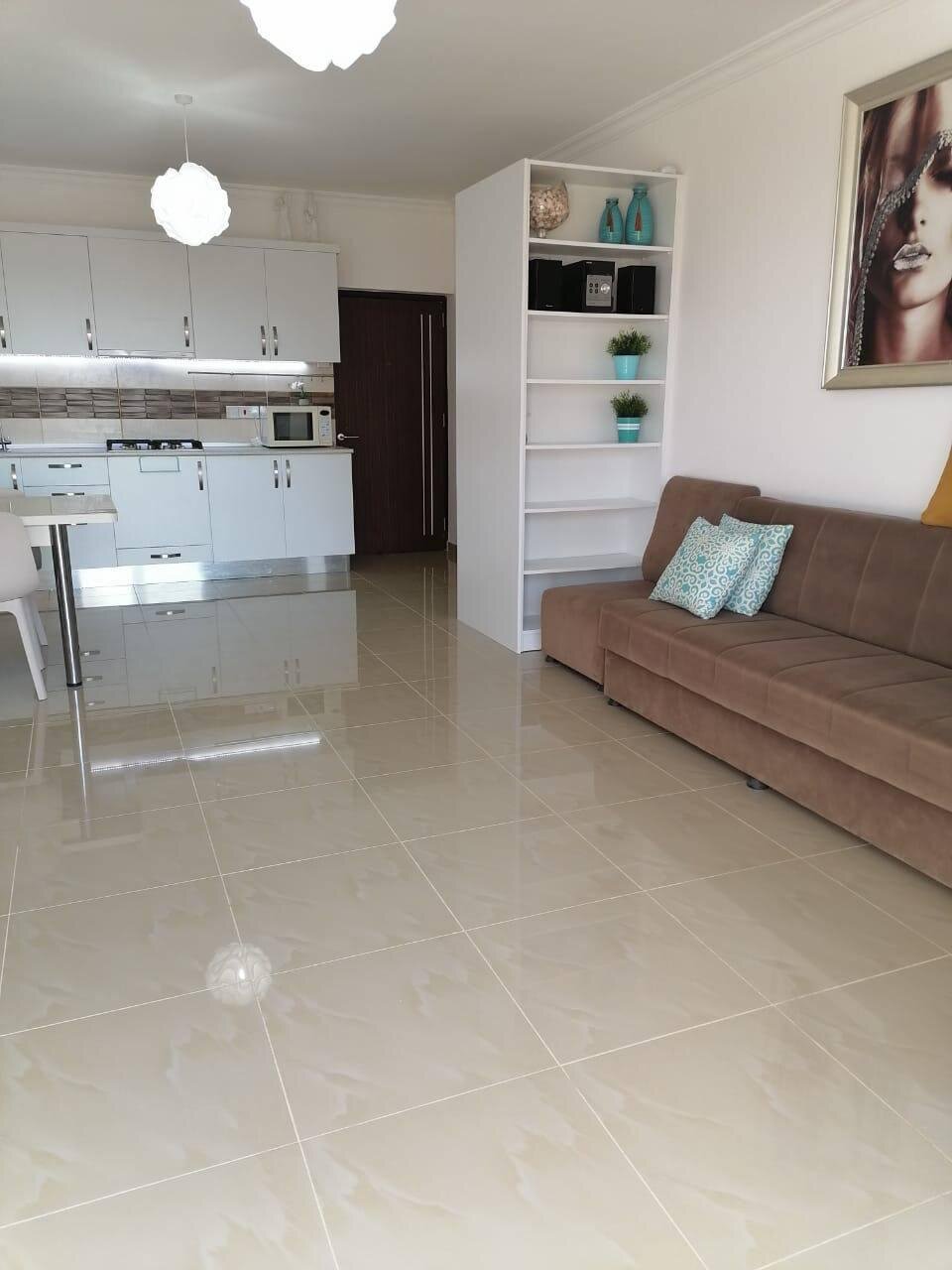 Living room and kitchen: a white shelving unit as a divider, a cushioned sofa and the kitchen behind