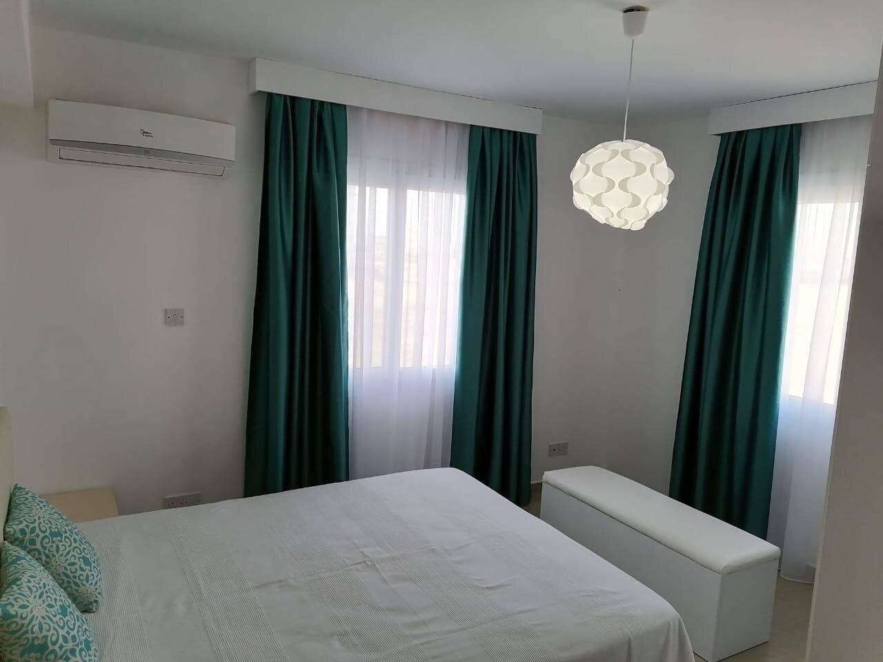 Bedroom with an air conditioner and two full-height windows with green curtains