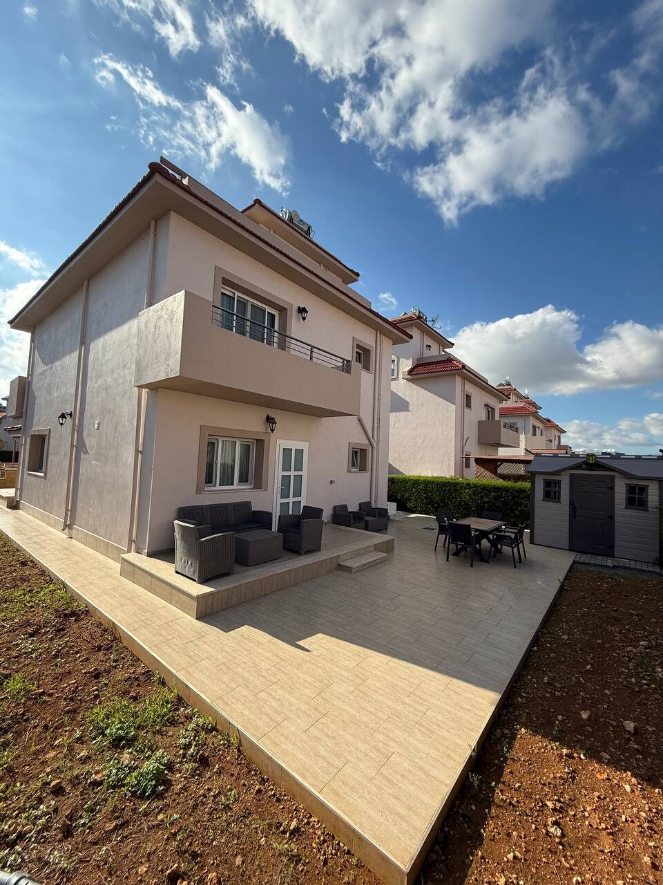 Side elevation of the villa and the paved yard with garden furniture