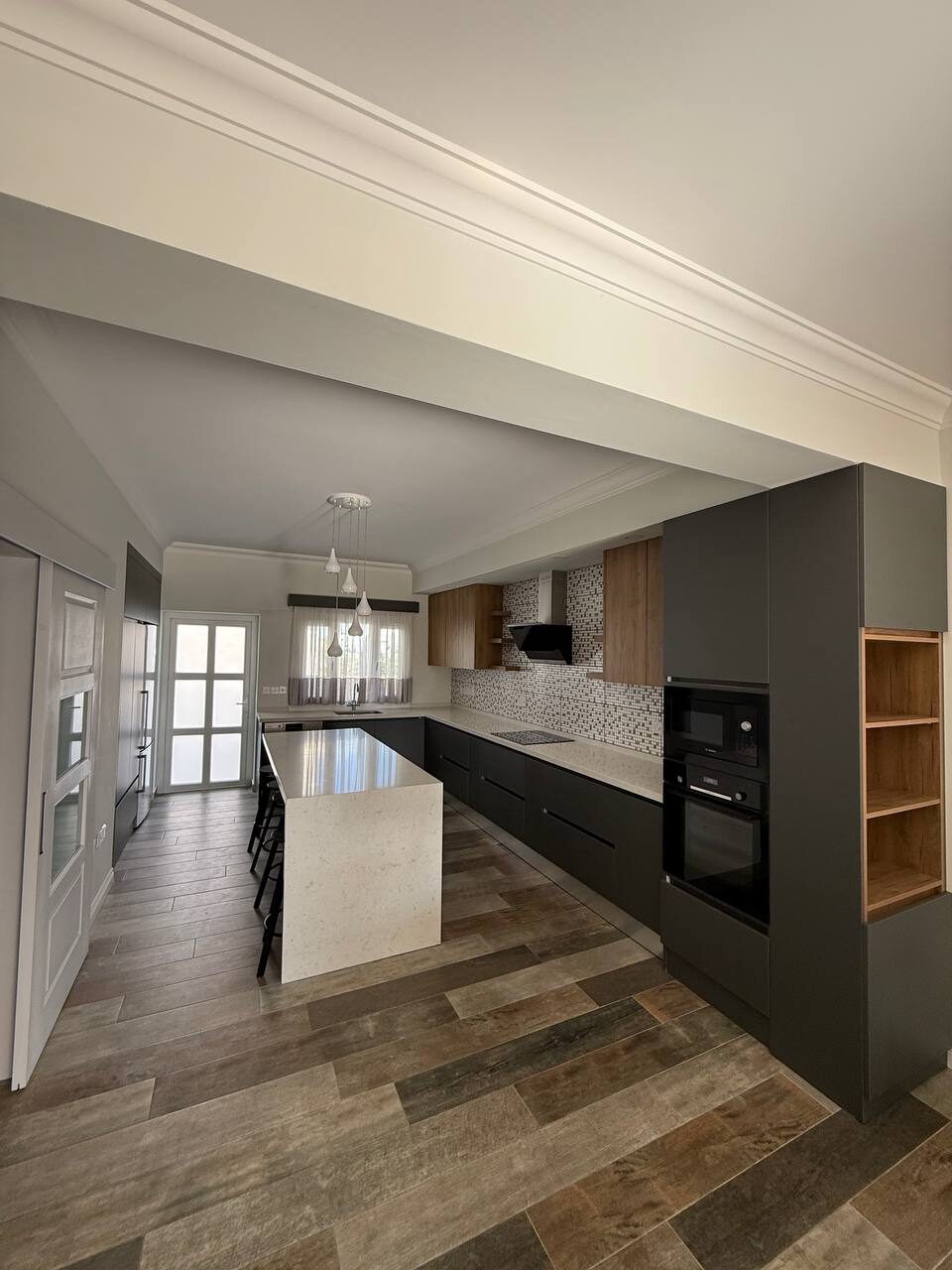 The kitchen seen from the living room: island and the built-in appliance column